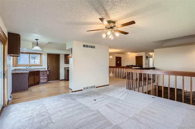 unfurnished room featuring a textured ceiling, light colored carpet, ceiling fan, and sink