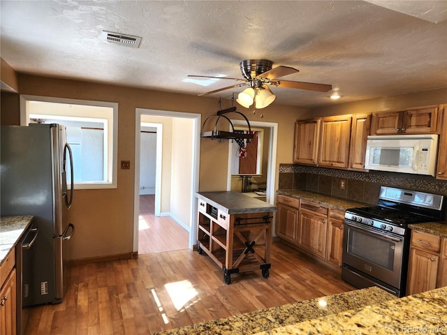 kitchen with ceiling fan, stainless steel appliances, backsplash, hardwood / wood-style floors, and a textured ceiling