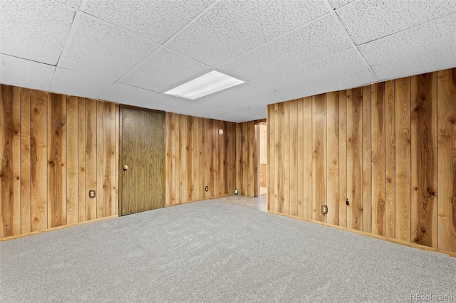 basement with a paneled ceiling, wooden walls, and carpet