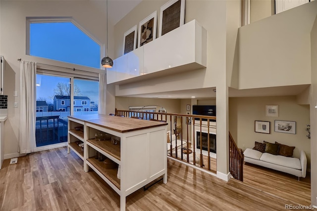 kitchen featuring a high ceiling, hanging light fixtures, light wood-type flooring, wood counters, and white cabinets