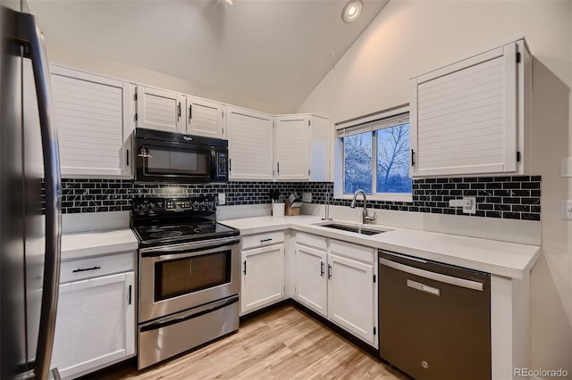 kitchen with lofted ceiling, light wood-type flooring, white cabinets, appliances with stainless steel finishes, and sink