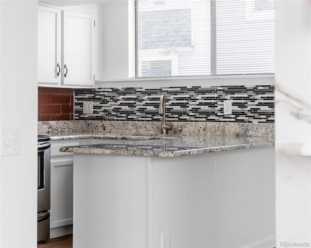 kitchen with sink, white cabinetry, tasteful backsplash, light stone counters, and stove