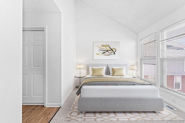 bedroom with lofted ceiling, hardwood / wood-style floors, and a textured ceiling