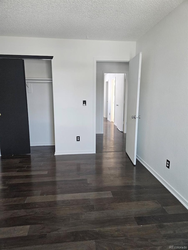 unfurnished bedroom featuring a closet, dark wood-style flooring, a textured ceiling, and baseboards