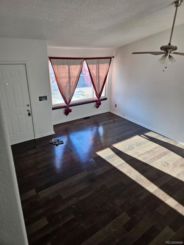 empty room with a textured ceiling, dark wood-style flooring, a ceiling fan, and baseboards