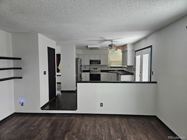 kitchen with dark wood finished floors, dark countertops, appliances with stainless steel finishes, white cabinets, and a peninsula