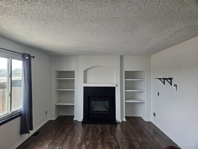 unfurnished living room featuring built in features, dark wood finished floors, and a textured ceiling