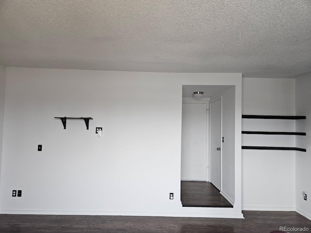 spare room featuring a textured ceiling, dark wood-style flooring, and baseboards