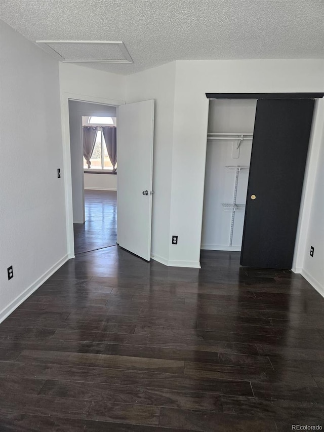 unfurnished bedroom with dark wood-style floors, a textured ceiling, baseboards, and a closet