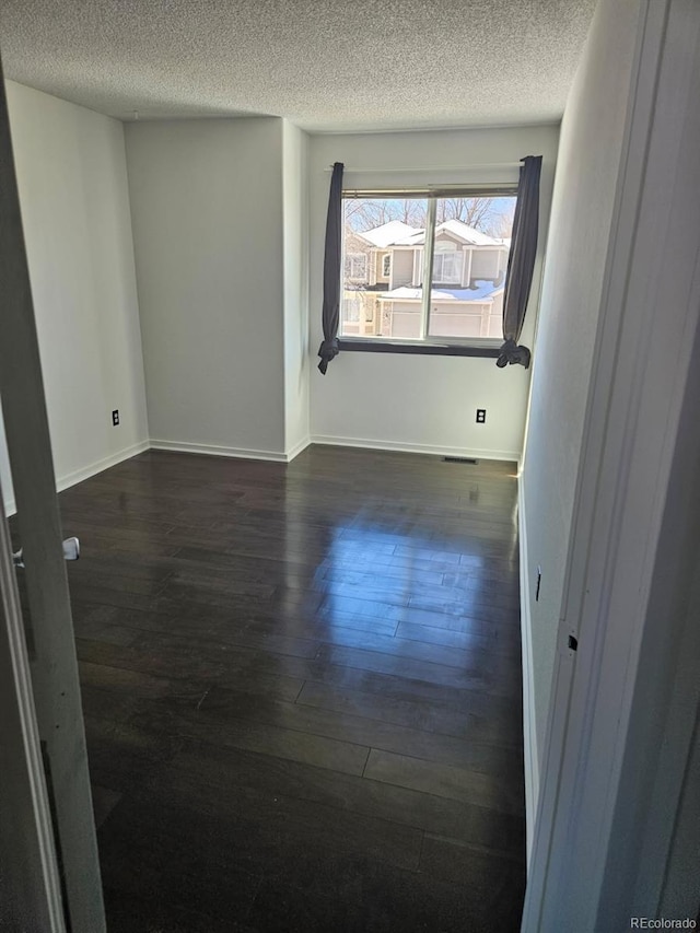 unfurnished room featuring dark wood-style floors, a textured ceiling, and baseboards