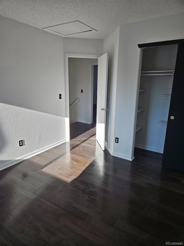 unfurnished bedroom featuring dark wood-style floors, a closet, baseboards, and a textured ceiling