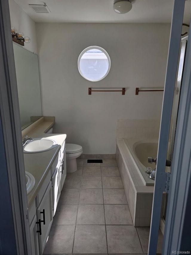 bathroom featuring toilet, a sink, tile patterned floors, double vanity, and tiled tub