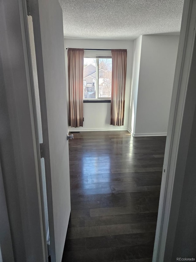 spare room with dark wood-style floors, a textured ceiling, and baseboards