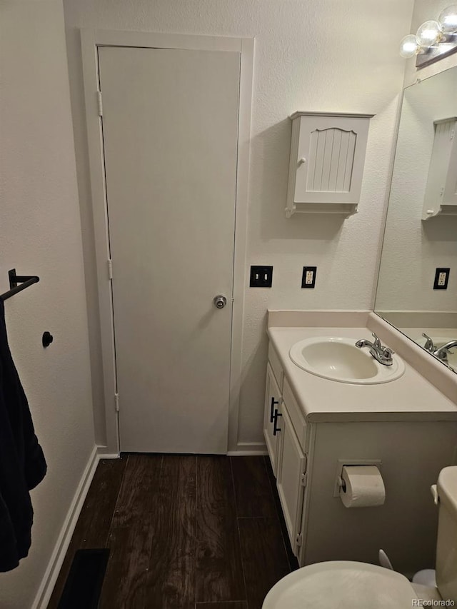 bathroom with toilet, baseboards, wood finished floors, and vanity