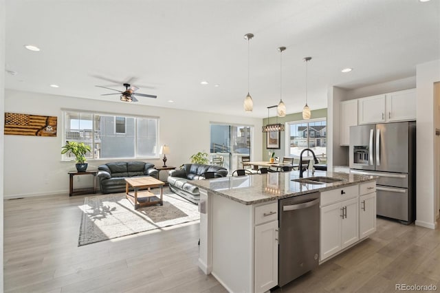 kitchen with appliances with stainless steel finishes, sink, white cabinets, light stone countertops, and a center island with sink