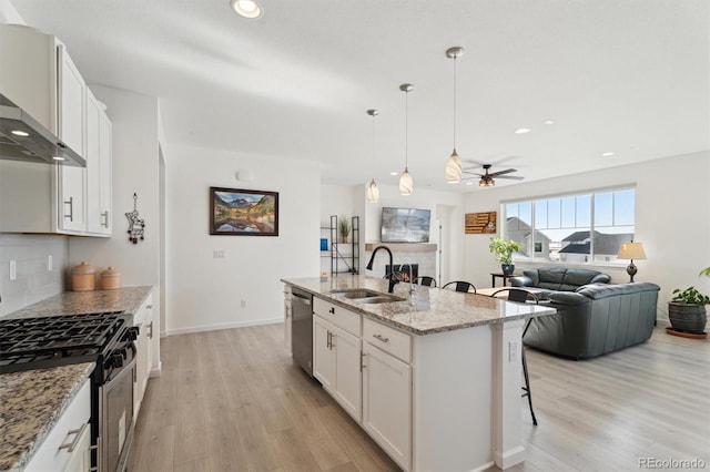 kitchen featuring light wood-style flooring, a sink, stainless steel appliances, a kitchen bar, and wall chimney range hood