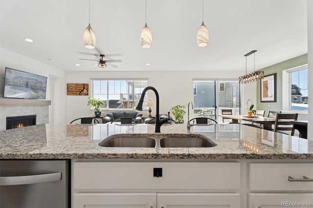 kitchen featuring light stone counters, a fireplace, a sink, white cabinetry, and open floor plan