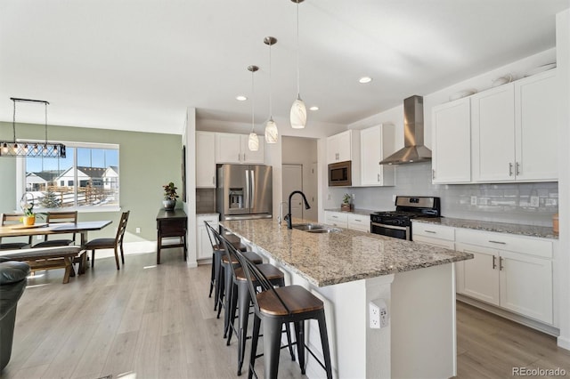 kitchen featuring a sink, stainless steel appliances, light wood-style floors, wall chimney exhaust hood, and tasteful backsplash