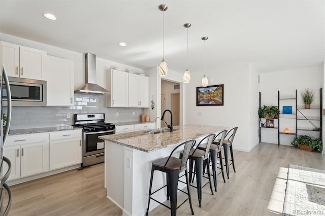 kitchen with light wood-style flooring, a sink, stainless steel appliances, wall chimney exhaust hood, and tasteful backsplash