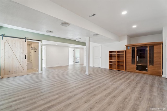 unfurnished living room with a barn door, baseboards, light wood-style floors, and visible vents