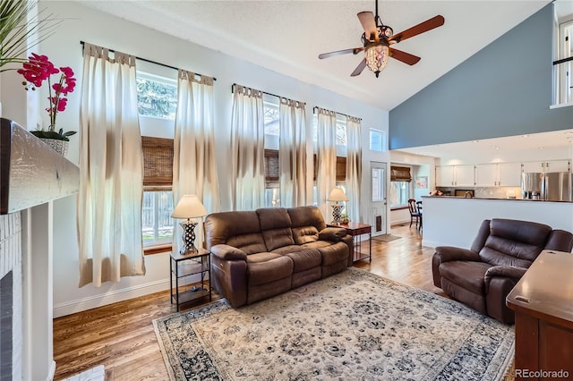 living room featuring plenty of natural light, high vaulted ceiling, ceiling fan, and light wood-type flooring