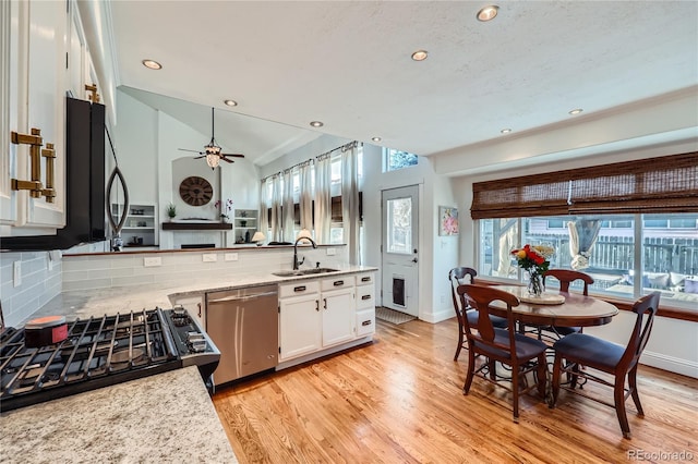 kitchen featuring sink, stainless steel dishwasher, white cabinets, light hardwood / wood-style floors, and backsplash