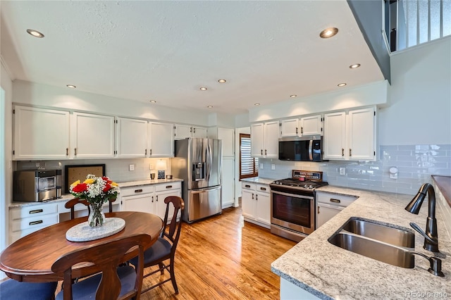 kitchen with sink, stainless steel appliances, light stone countertops, white cabinets, and light wood-type flooring