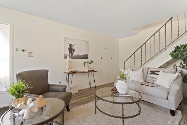 living room with stairway, a textured ceiling, baseboards, and wood finished floors