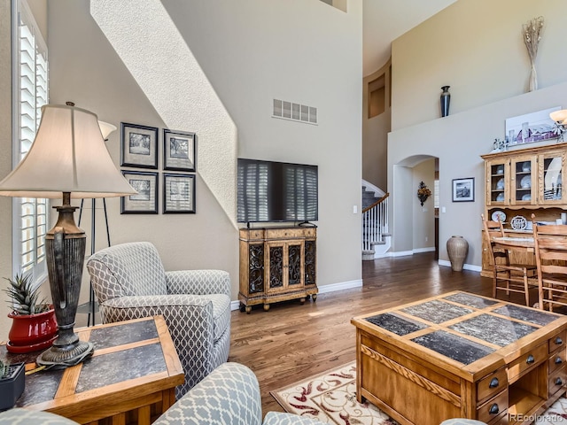 11074 Grayledge Cir, Highlands Ranch, CO 80130 - living room featuring arched walkways, stairs, a towering ceiling, wood finished floors, and plenty of natural light