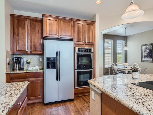 11074 Grayledge Cir, Highlands Ranch, CO 80130 - kitchen featuring stainless steel appliances, wood finished floors, arched walkways, light stone countertops, and decorative light fixtures
