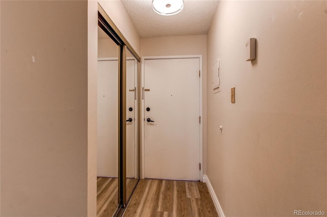 doorway with a textured ceiling, light wood-type flooring, and baseboards