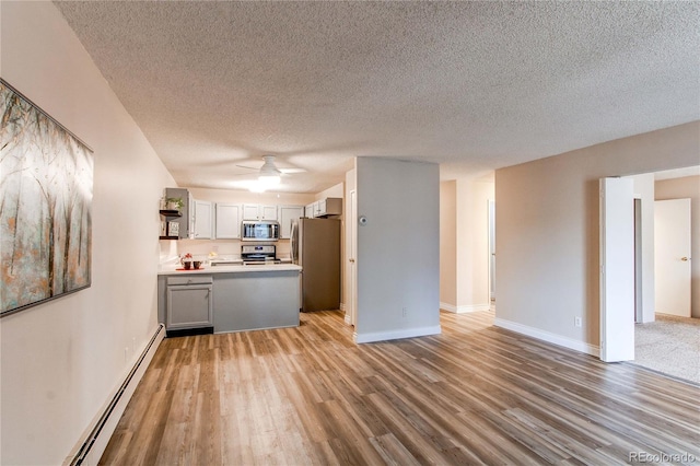 kitchen featuring open floor plan, stainless steel appliances, baseboard heating, and light wood-style flooring