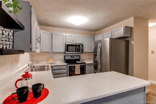 kitchen with stainless steel appliances, tasteful backsplash, light countertops, a sink, and a peninsula