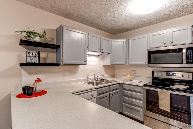 kitchen with stainless steel appliances, a sink, gray cabinets, open shelves, and tasteful backsplash