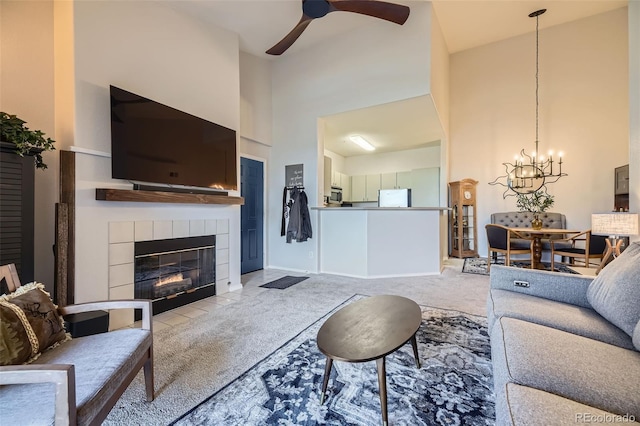 carpeted living room with a tiled fireplace, a towering ceiling, and ceiling fan with notable chandelier