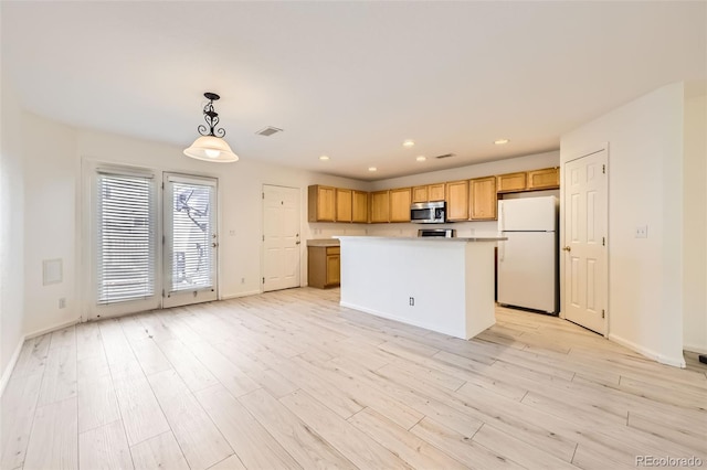 kitchen with a kitchen island, hanging light fixtures, white fridge, and light hardwood / wood-style flooring