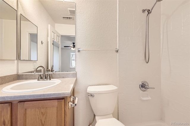 bathroom with tiled shower, toilet, a textured ceiling, vanity, and ceiling fan