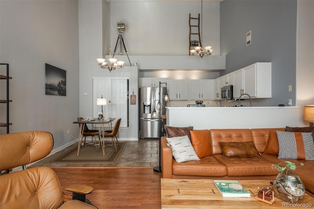 living room with wood finished floors, baseboards, an inviting chandelier, and a towering ceiling