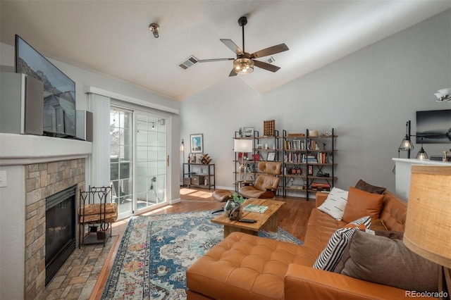 living room featuring visible vents, baseboards, ceiling fan, vaulted ceiling, and a stone fireplace