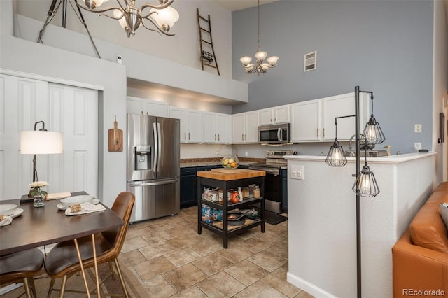 kitchen featuring visible vents, appliances with stainless steel finishes, a towering ceiling, a notable chandelier, and white cabinetry