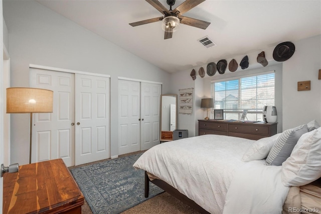 bedroom with visible vents, carpet floors, lofted ceiling, ceiling fan, and multiple closets