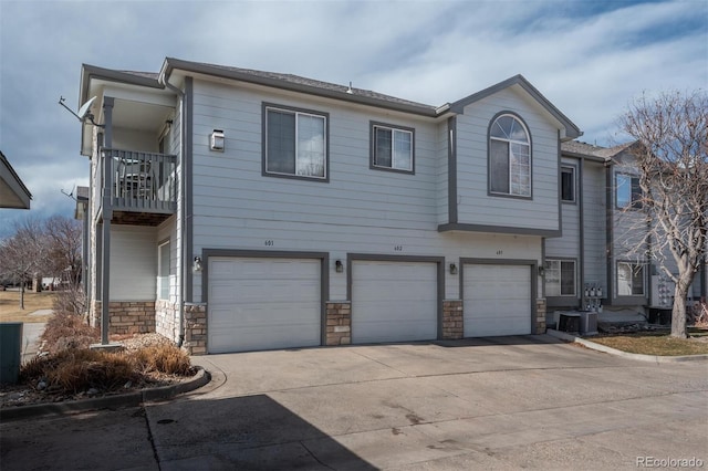 view of property featuring stone siding, concrete driveway, an attached garage, a balcony, and central AC unit