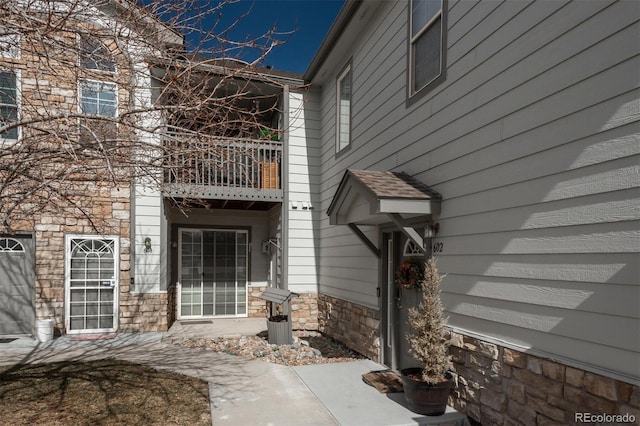 view of exterior entry featuring stone siding and a balcony