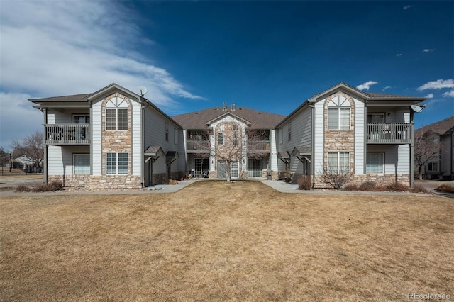 view of front facade with a front yard, a balcony, and stone siding