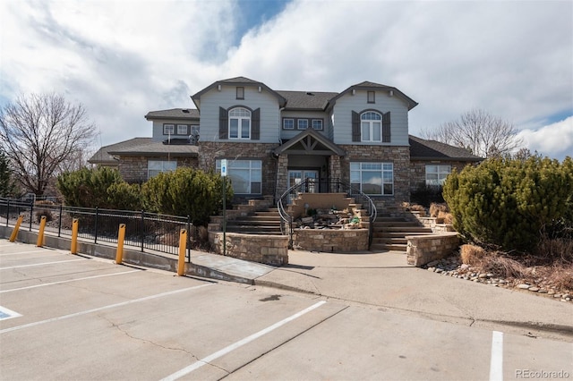 view of front of home featuring a fenced front yard, stone siding, and uncovered parking