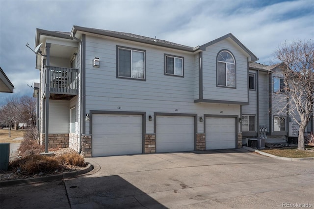 view of front of house with stone siding, driveway, a garage, and a balcony