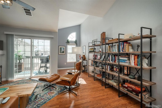 living area featuring wood finished floors, visible vents, vaulted ceiling, a ceiling fan, and baseboards