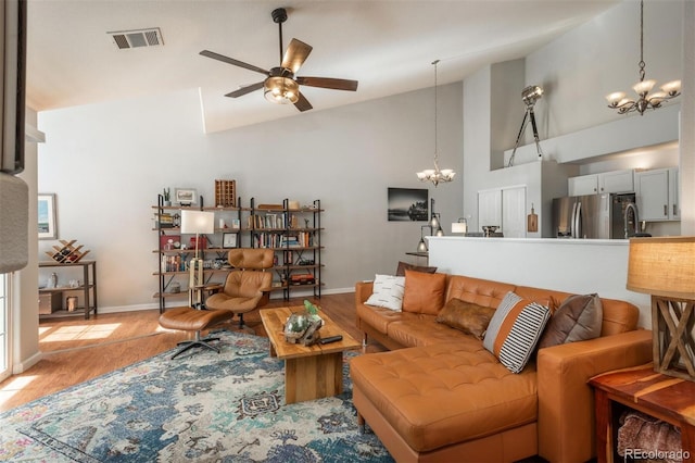living area featuring light wood-style flooring, baseboards, visible vents, ceiling fan with notable chandelier, and high vaulted ceiling