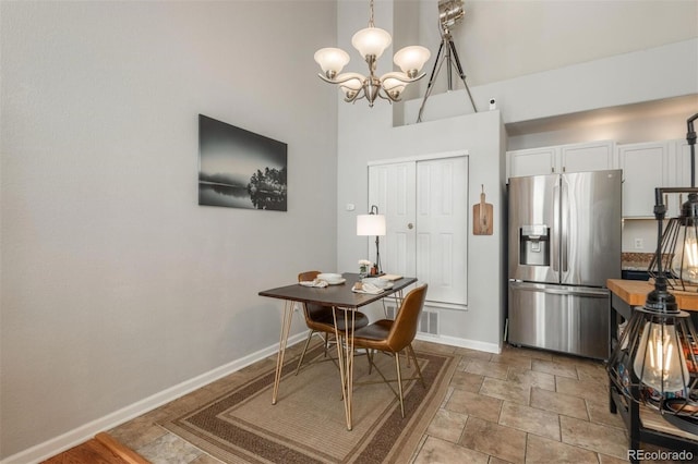 dining space with a high ceiling, stone finish floor, visible vents, baseboards, and a chandelier
