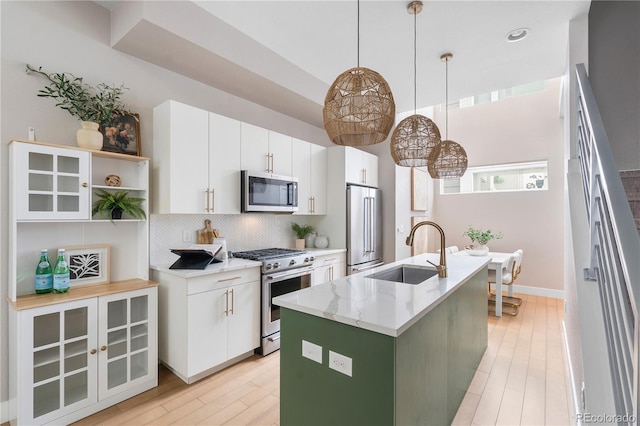 kitchen with appliances with stainless steel finishes, pendant lighting, white cabinetry, an island with sink, and sink